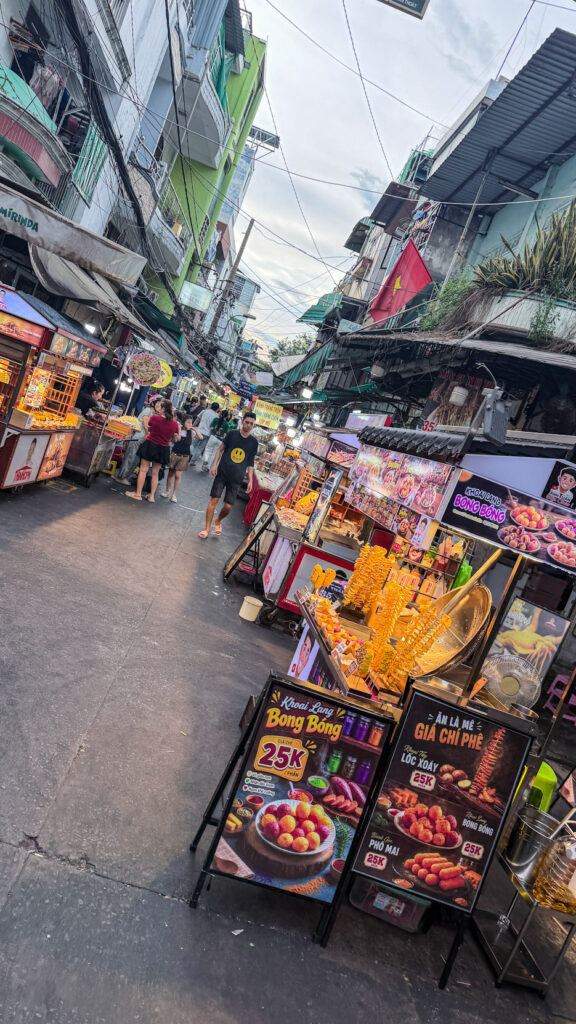 Hồ Thị Kỷ street food alley with grilled chicken and vendors beside the flower market Saigon