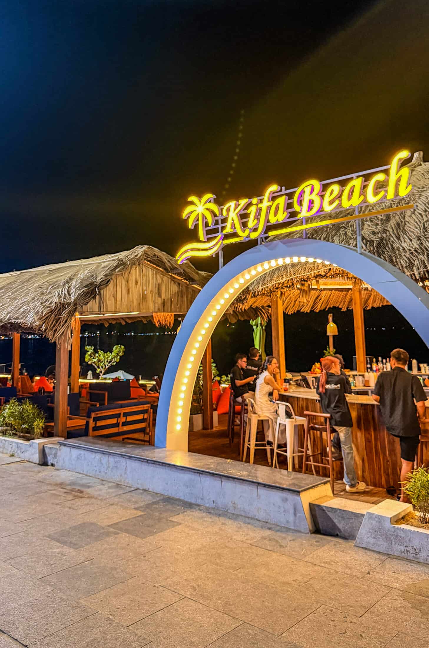 Neon sign and thatched bar at night at Kifa Beach, Quy Nhon