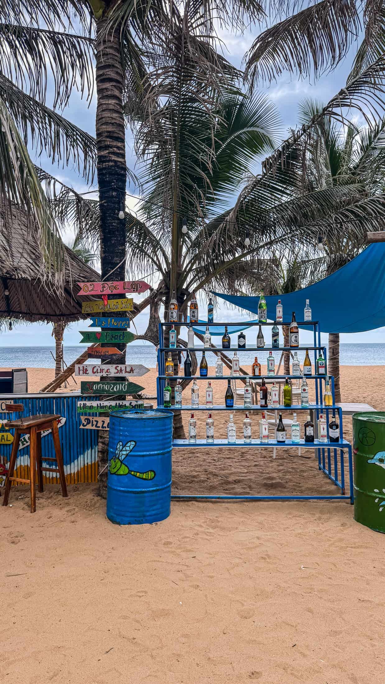 Bottle display shelf and painted oil drums on the sand at Sala TuyHoa Beach Club