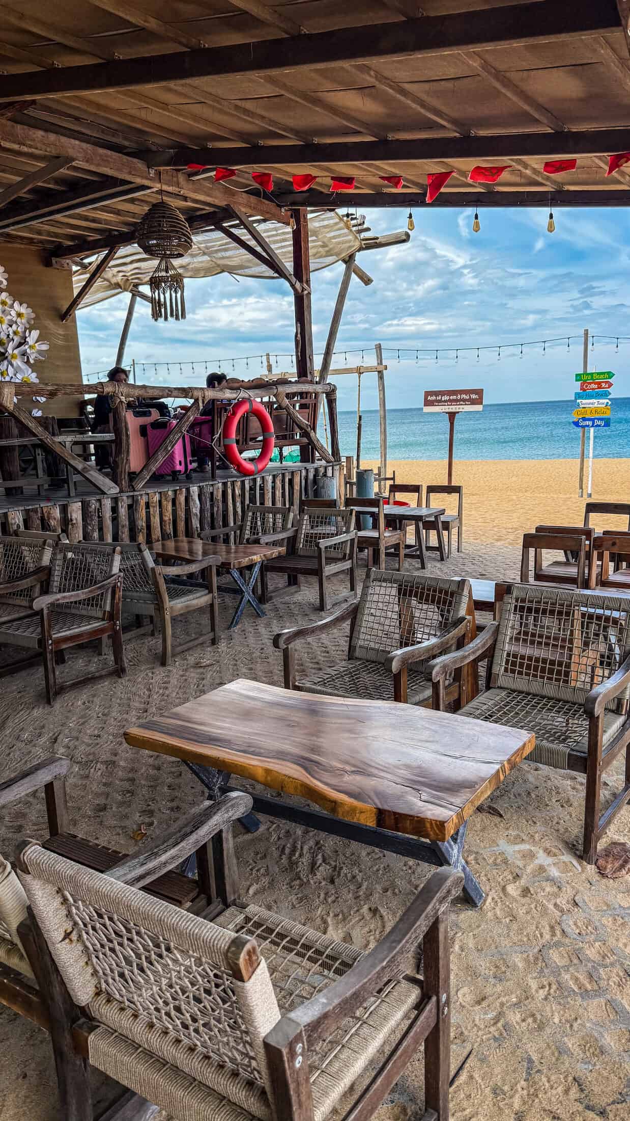 Woven rope armchairs and a live-edge wood table on the sand at URA Beach Camping & Coffee