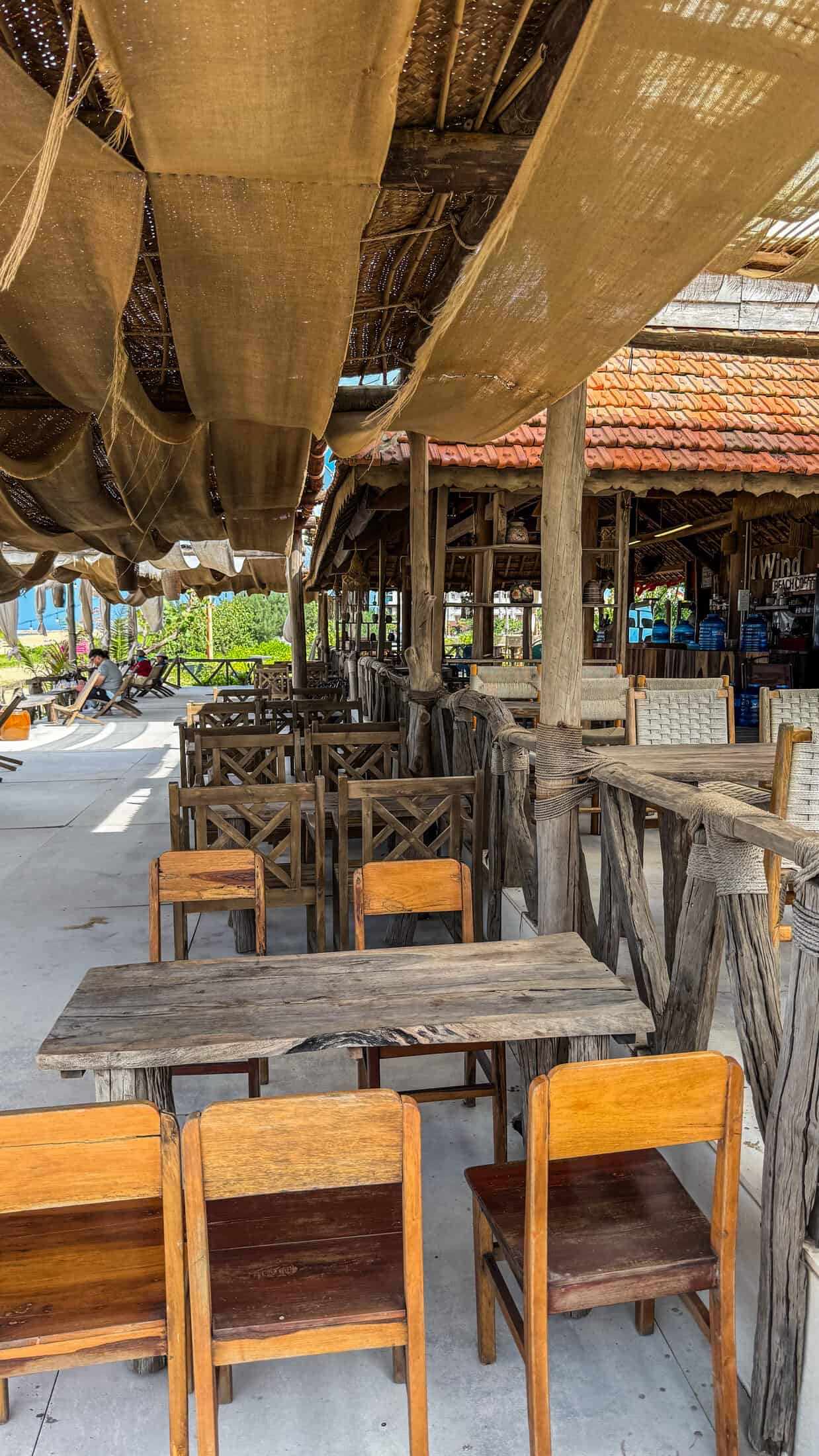 Rustic driftwood tables under a burlap canopy at Wild Wind Beach Coffee, Tuy Hoa